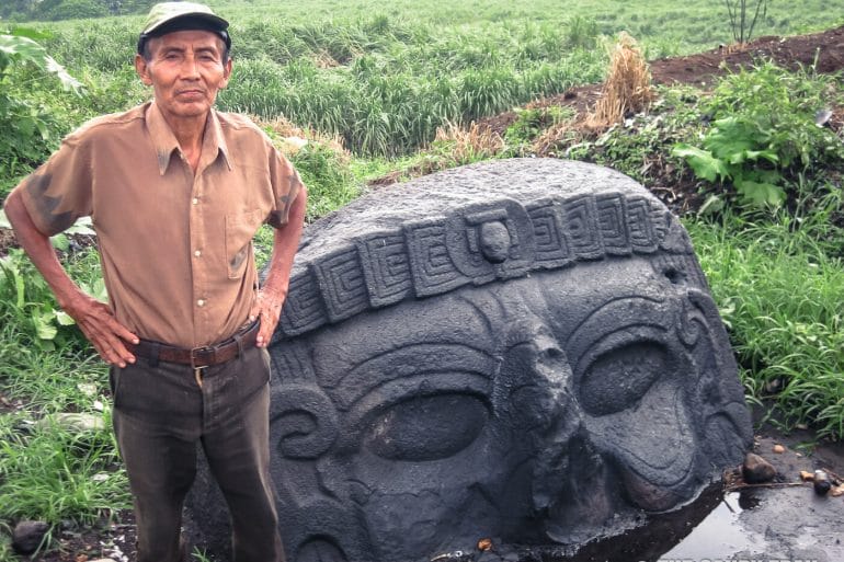 sugarcane worker beside giant stone head guatemala