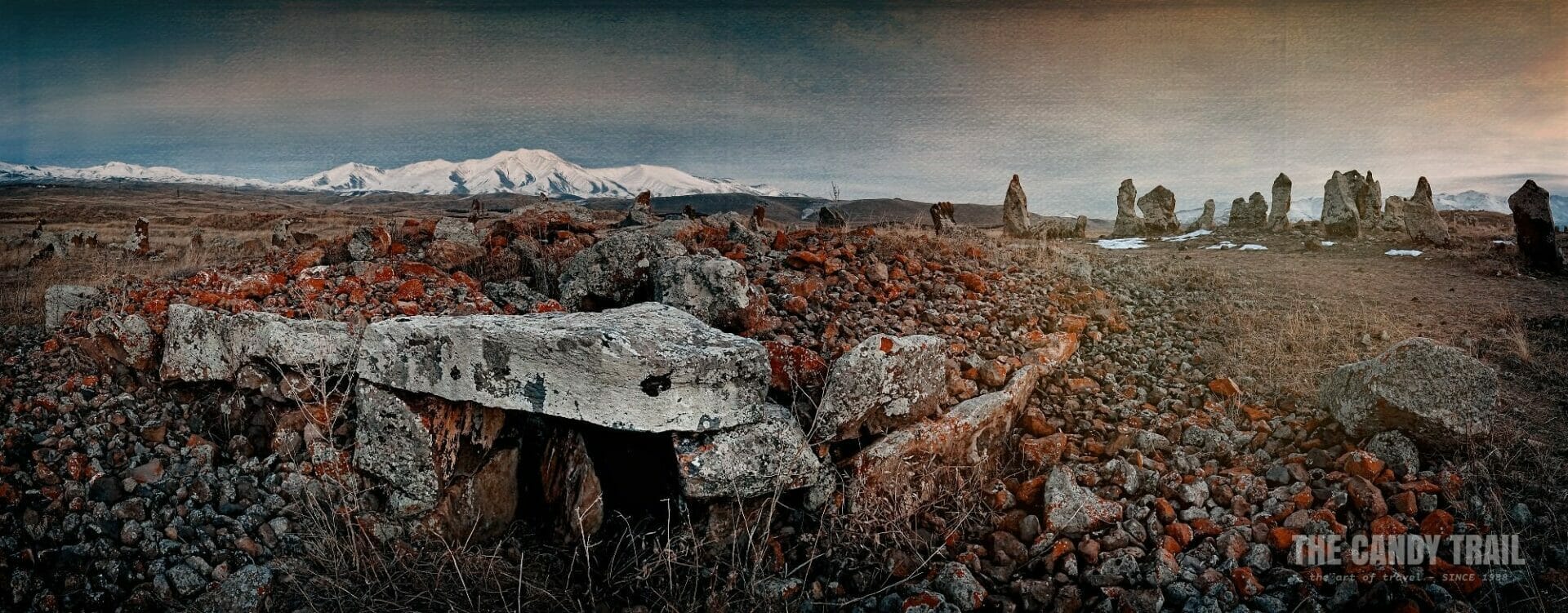 Zorats Karer stone circle in Armenia amid a snowy mountain panorama.