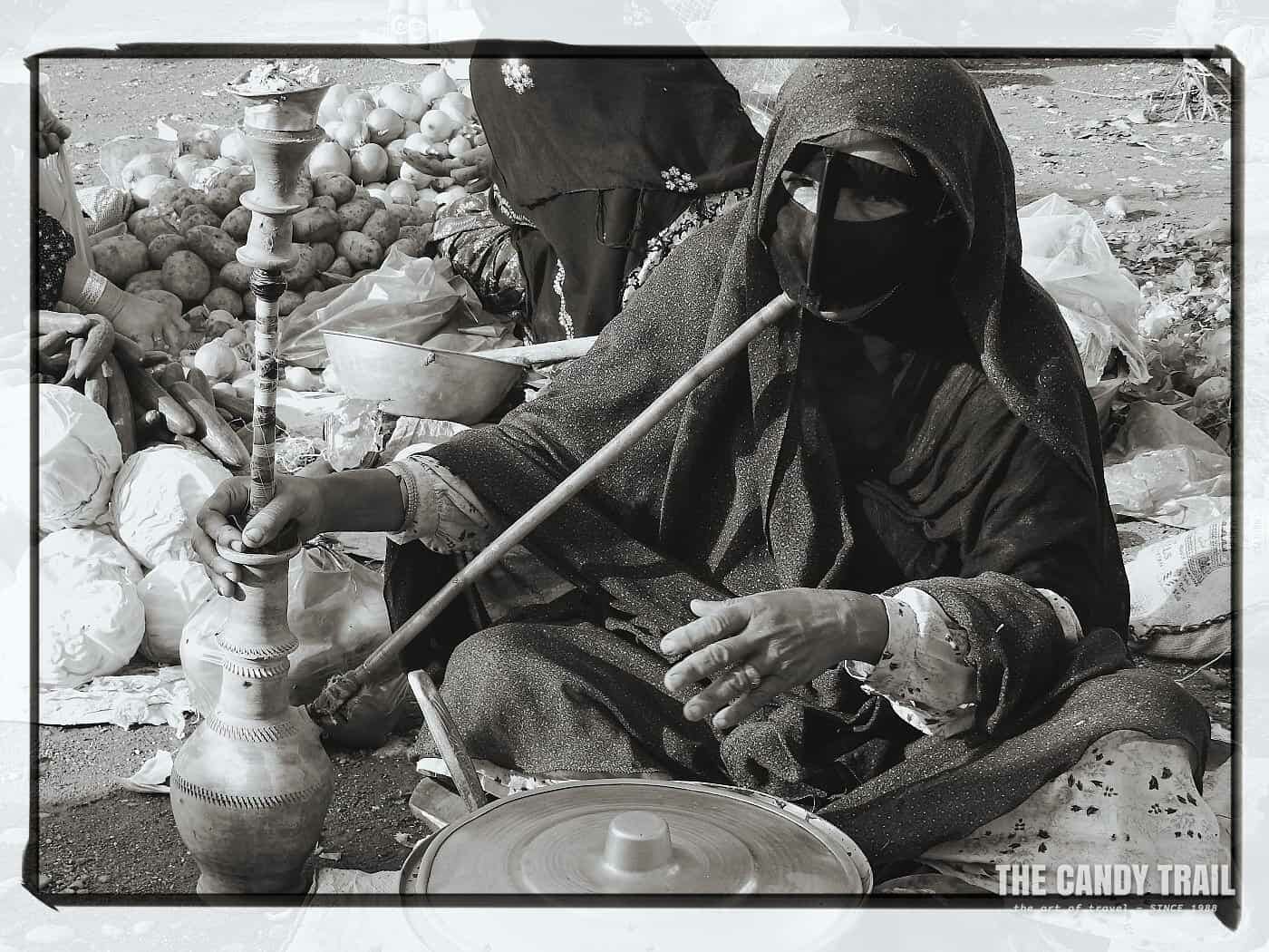 elderly masked woman with traditional hookah smoking pipe in Iran