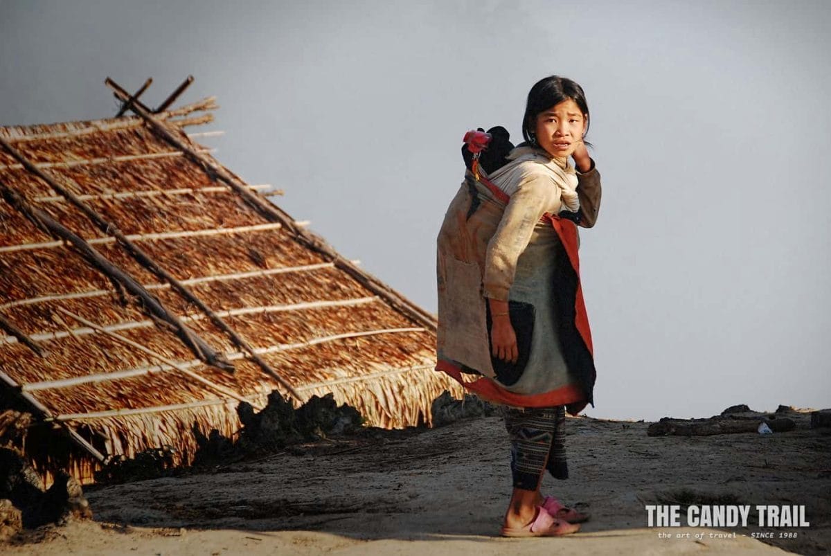 Young Akha tribe girl carrying her sister on her back in Laos.