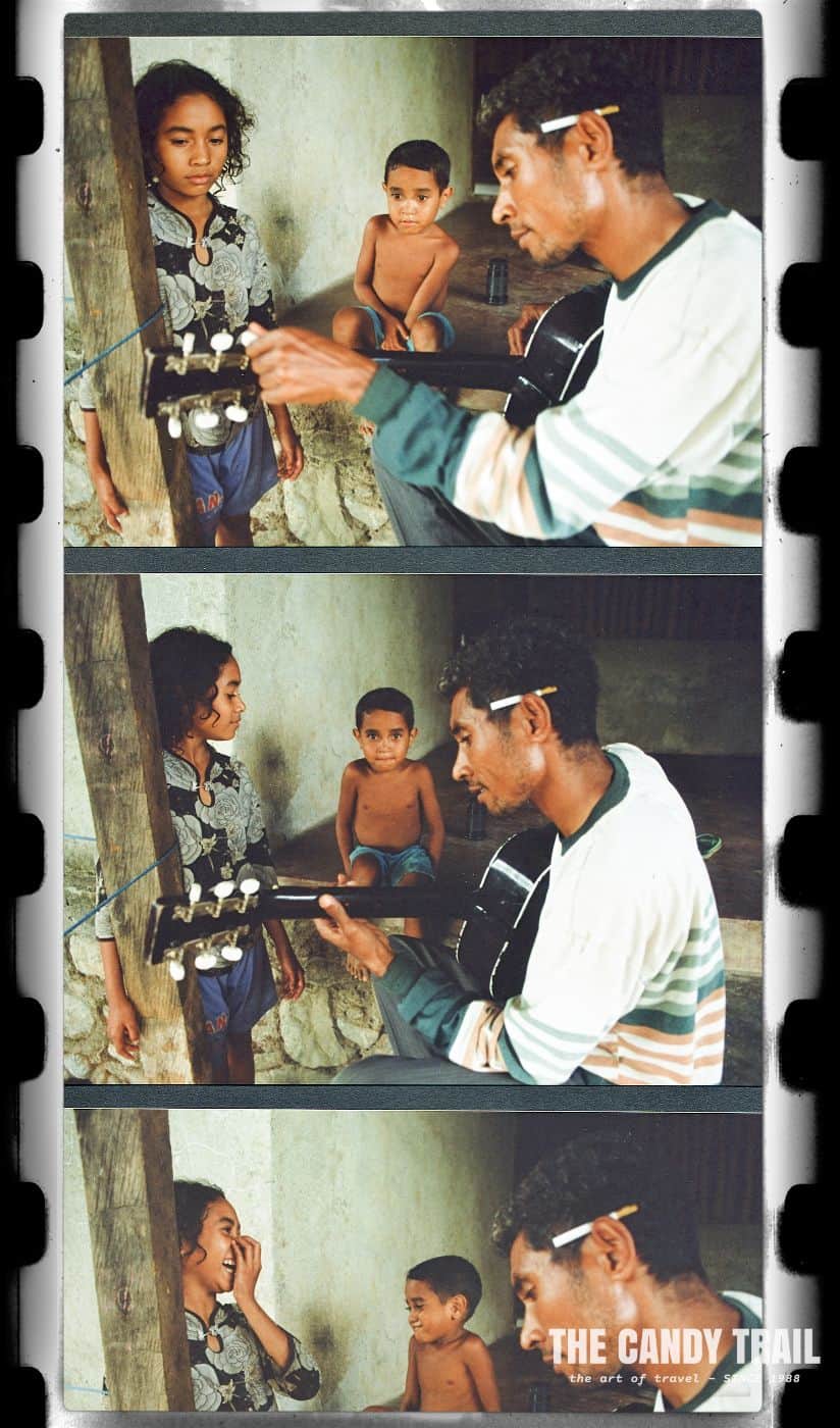 man playing guitar to kids in ainaro east timor 2000