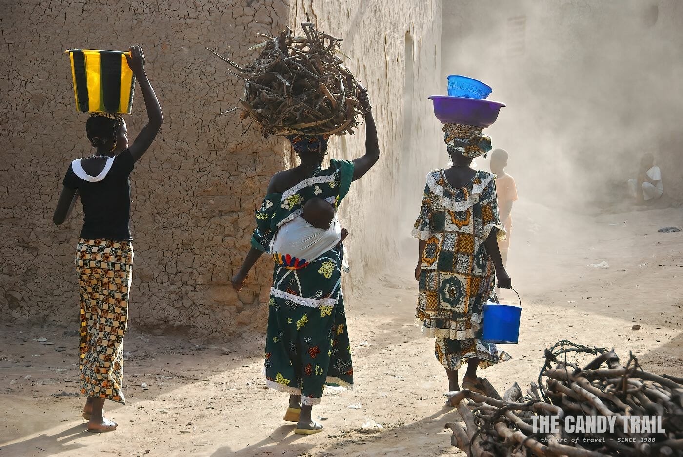 women carry wares on head in dusty backstreets of old Djenne.